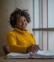 A student sits at a table near a window at 51Ivany Campus and smiles at the camera.